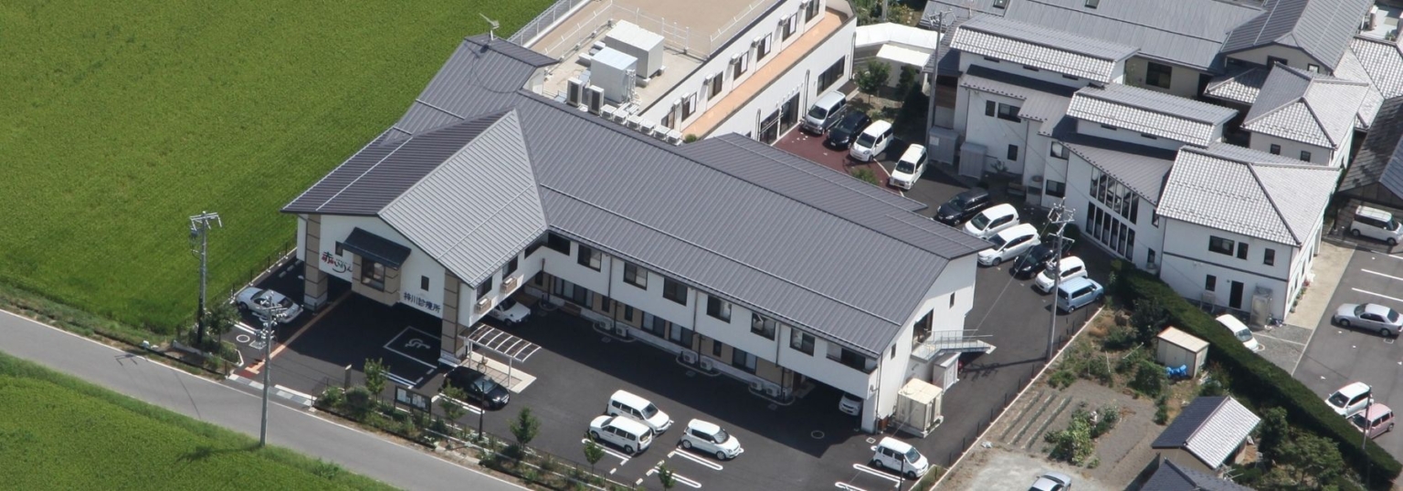 介護施設の空撮写真。駐車場と建物外観が見える上空からの眺め。